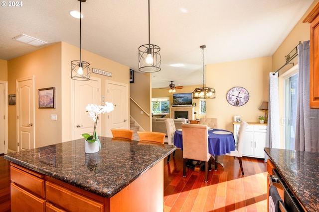 kitchen featuring hanging light fixtures, ceiling fan, dark stone counters, dark hardwood / wood-style floors, and a center island