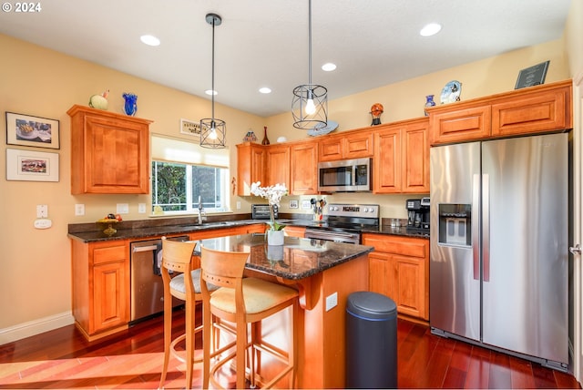 kitchen with appliances with stainless steel finishes, a center island, dark wood-type flooring, sink, and decorative light fixtures