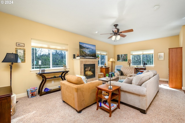 living room with ceiling fan, a tile fireplace, and light colored carpet