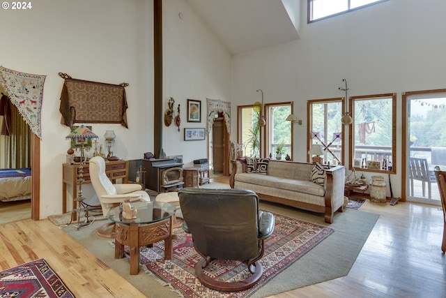 living room featuring a wood stove, light hardwood / wood-style flooring, a healthy amount of sunlight, and a high ceiling