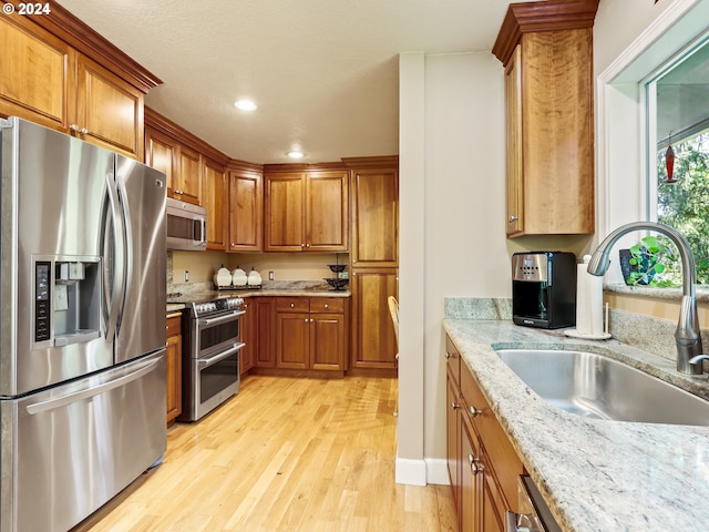 kitchen with recessed lighting, light wood-style flooring, brown cabinetry, stainless steel appliances, and a sink