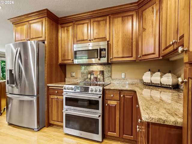 kitchen with light wood-style floors, brown cabinets, light stone counters, and appliances with stainless steel finishes