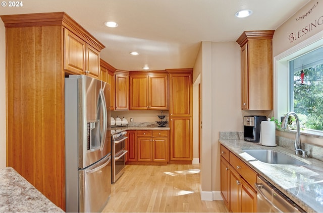 kitchen featuring light stone countertops, a sink, stainless steel appliances, brown cabinets, and light wood finished floors