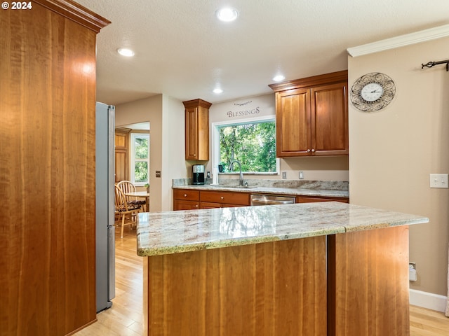 kitchen with light stone countertops, appliances with stainless steel finishes, a sink, brown cabinets, and light wood finished floors