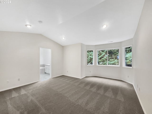 spare room featuring dark colored carpet and vaulted ceiling