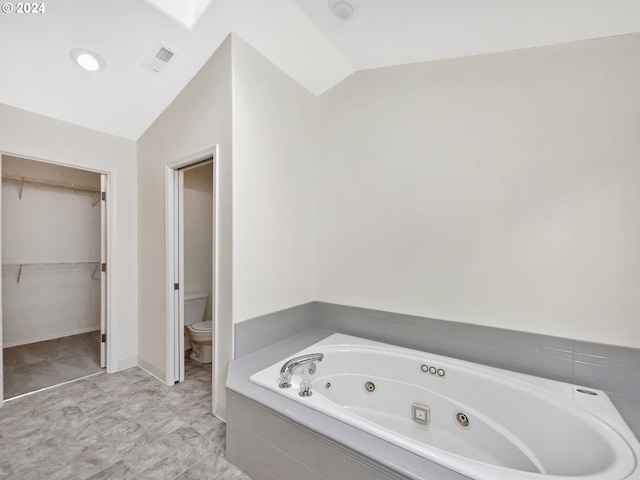 bathroom with toilet, lofted ceiling, and tiled bath