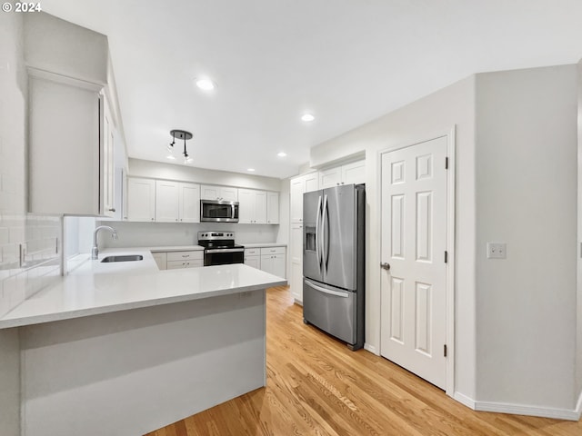 kitchen featuring appliances with stainless steel finishes, sink, kitchen peninsula, white cabinetry, and light hardwood / wood-style flooring