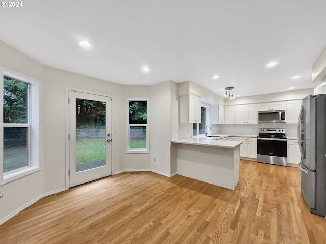 kitchen featuring kitchen peninsula, white cabinetry, light hardwood / wood-style flooring, sink, and stainless steel appliances