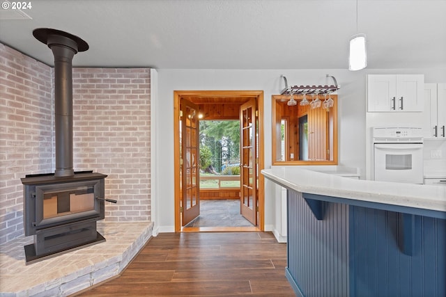 3735 NE Surf Dr, Lincoln City, OR 97367 - kitchen with white oven, dark wood-type flooring, a wood stove, white cabinets, and decorative light fixtures