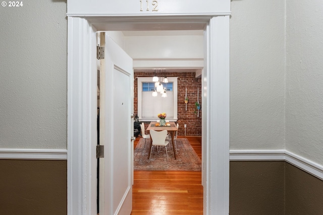 hall with an inviting chandelier, light hardwood / wood-style flooring, and brick wall