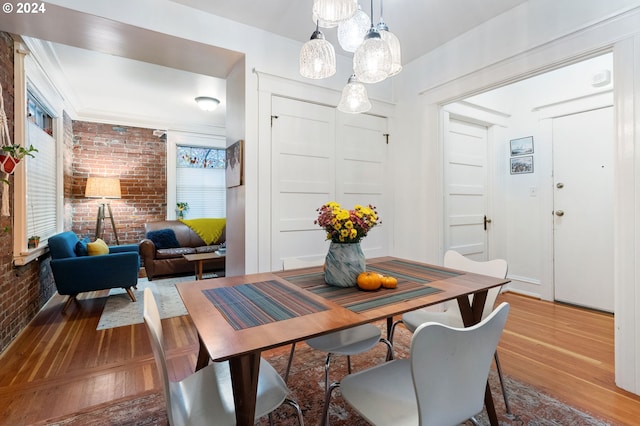 dining area featuring hardwood / wood-style floors, ornamental molding, and brick wall