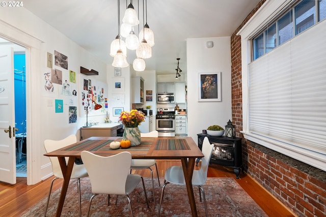 dining area featuring dark hardwood / wood-style flooring, an inviting chandelier, and brick wall