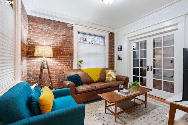 living room featuring french doors, light wood-type flooring, ornamental molding, and brick wall