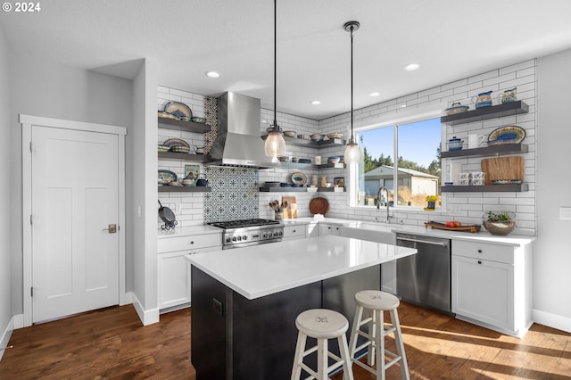 kitchen with a kitchen island, a kitchen breakfast bar, stainless steel appliances, sink, and wall chimney range hood