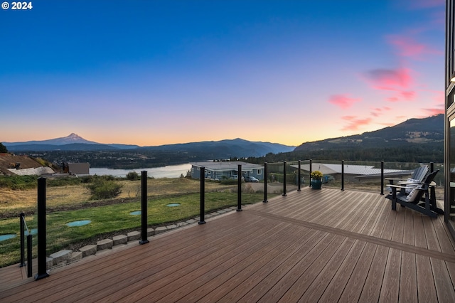 deck at dusk featuring a water and mountain view and a yard