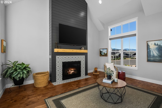 living room with high vaulted ceiling, a tiled fireplace, and wood-type flooring