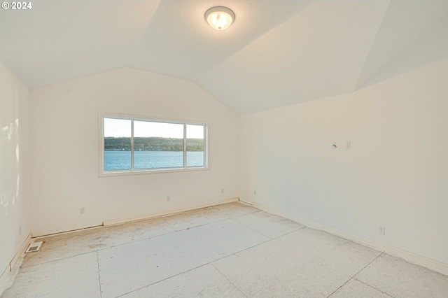 empty room featuring a textured ceiling, a water view, and lofted ceiling