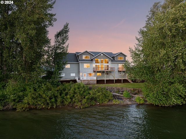 back house at dusk featuring a balcony and a water view