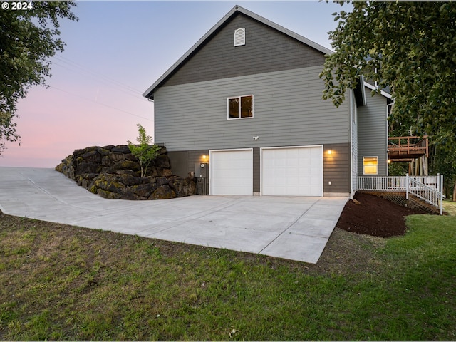 property exterior at dusk with a wooden deck, a yard, and a garage