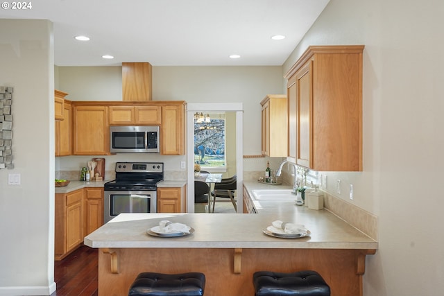 kitchen featuring sink, dark hardwood / wood-style floors, kitchen peninsula, a breakfast bar, and appliances with stainless steel finishes