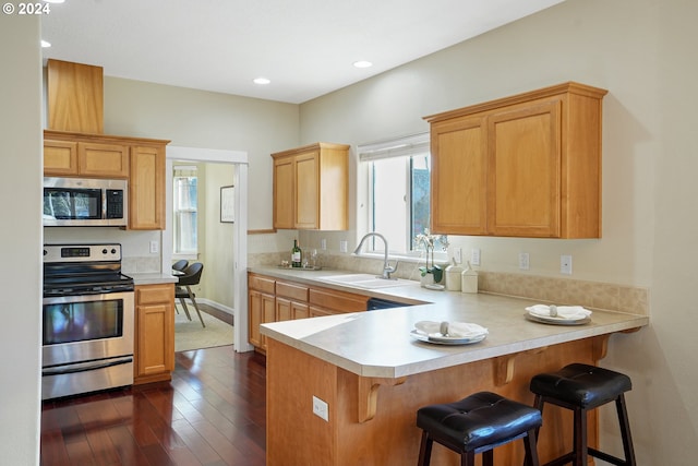 kitchen with kitchen peninsula, appliances with stainless steel finishes, dark hardwood / wood-style flooring, sink, and a breakfast bar area