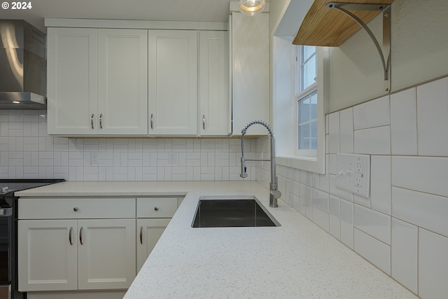 kitchen featuring white cabinetry, sink, wall chimney exhaust hood, tasteful backsplash, and range