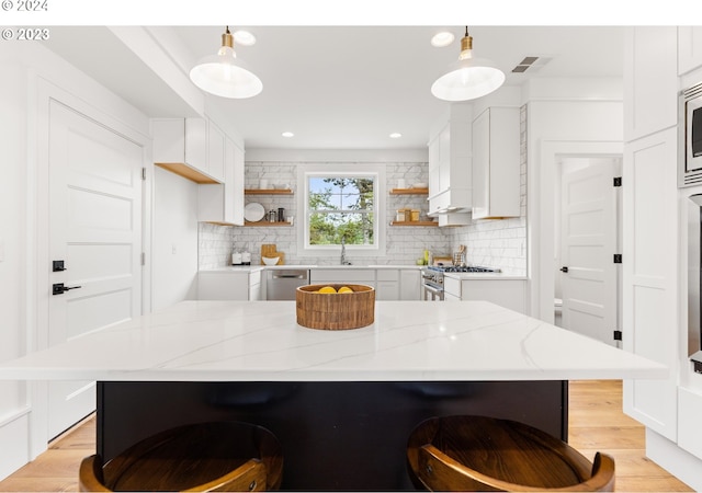 kitchen with backsplash, stainless steel appliances, light hardwood / wood-style floors, and decorative light fixtures