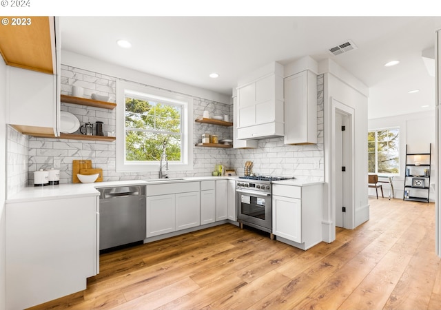 kitchen with backsplash, appliances with stainless steel finishes, light hardwood / wood-style flooring, and white cabinetry