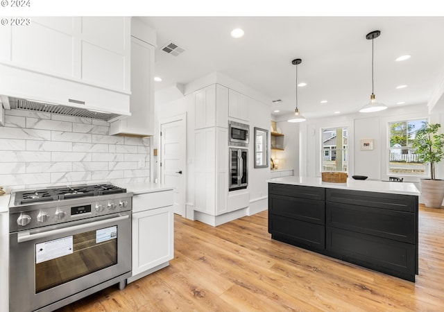 kitchen with light hardwood / wood-style flooring, white cabinetry, appliances with stainless steel finishes, custom range hood, and a kitchen island