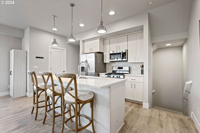 kitchen with pendant lighting, white cabinets, light wood-type flooring, an island with sink, and appliances with stainless steel finishes