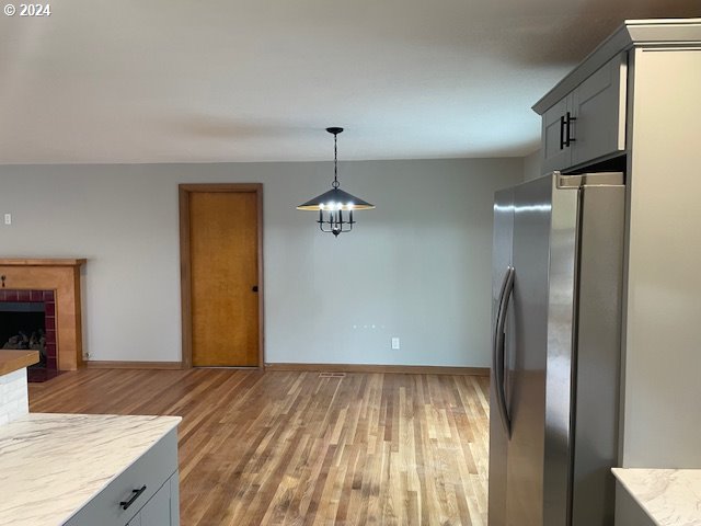 kitchen with a tile fireplace, pendant lighting, hardwood / wood-style floors, gray cabinets, and stainless steel refrigerator