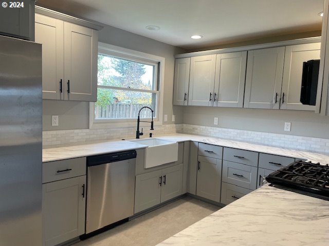 kitchen featuring gray cabinetry, sink, stainless steel appliances, light stone counters, and decorative backsplash