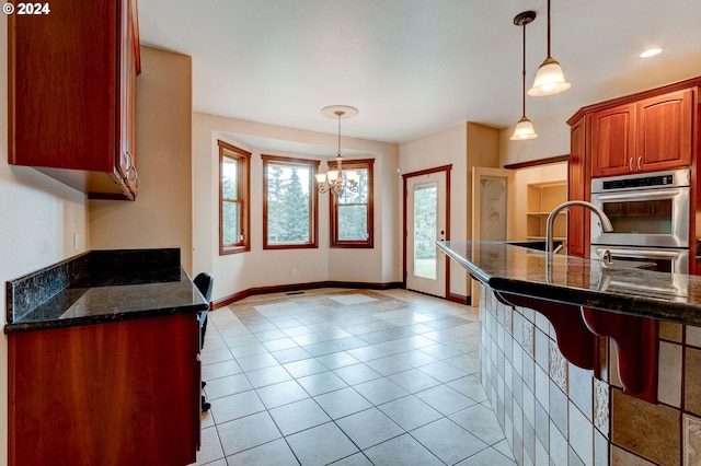 kitchen featuring double oven, hanging light fixtures, a chandelier, and dark stone counters