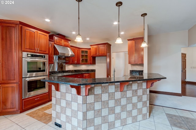 kitchen featuring range hood, hanging light fixtures, stainless steel appliances, dark stone counters, and a kitchen breakfast bar