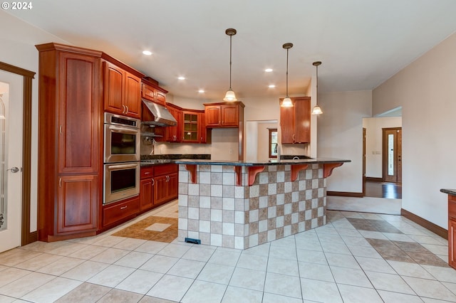 kitchen with pendant lighting, dark stone counters, light tile patterned floors, double oven, and a breakfast bar area