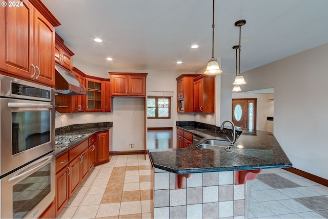 kitchen with dark stone counters, stainless steel appliances, decorative light fixtures, a kitchen breakfast bar, and sink