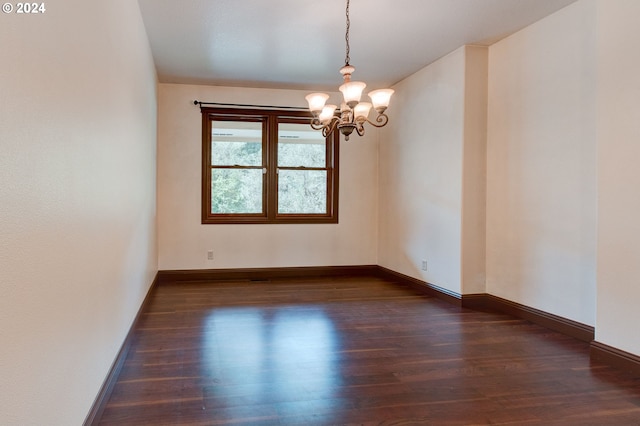 spare room featuring dark wood-type flooring and an inviting chandelier