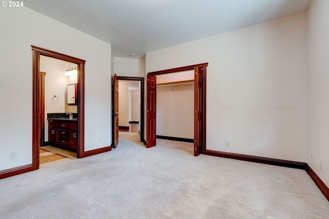 unfurnished bedroom featuring light carpet, a textured ceiling, connected bathroom, sink, and a closet