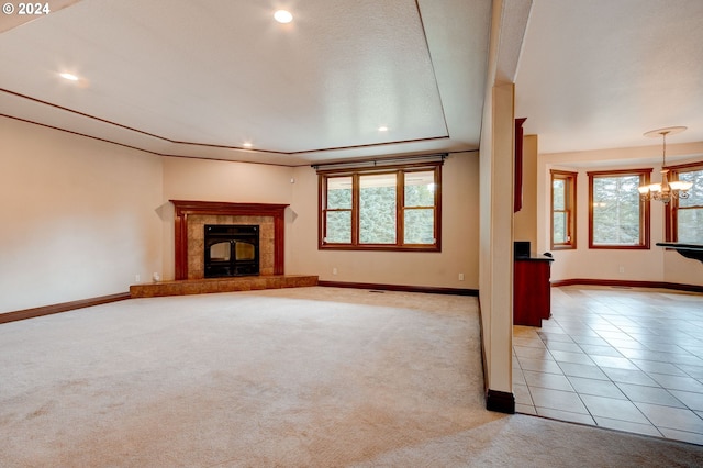 unfurnished living room featuring a tiled fireplace, a chandelier, light carpet, a tray ceiling, and a textured ceiling