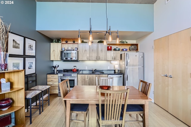 kitchen featuring sink, stainless steel appliances, a high ceiling, pendant lighting, and light wood-type flooring