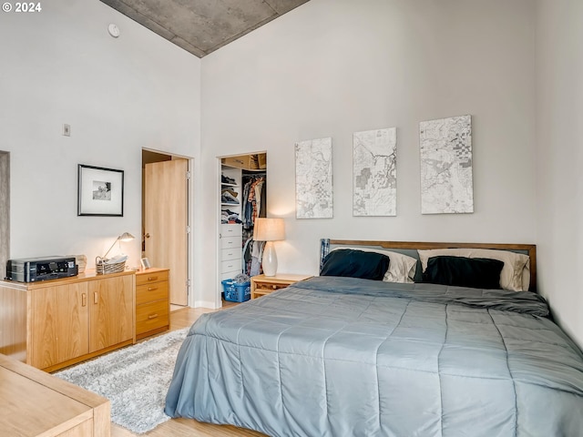 bedroom with light hardwood / wood-style floors, a spacious closet, a high ceiling, and a closet