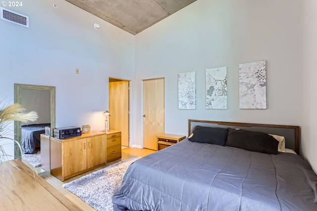 bedroom with a towering ceiling and light hardwood / wood-style floors