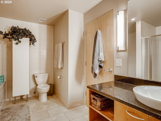 bathroom with vanity, a shower with door, tile patterned flooring, toilet, and tile walls