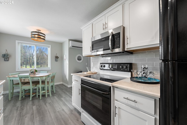 kitchen featuring black refrigerator, a wall mounted air conditioner, electric range, light hardwood / wood-style flooring, and white cabinetry