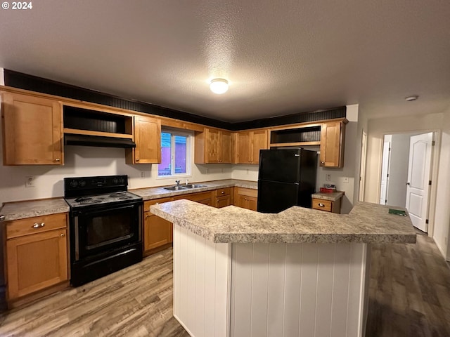 kitchen featuring black appliances, sink, light wood-type flooring, a textured ceiling, and kitchen peninsula