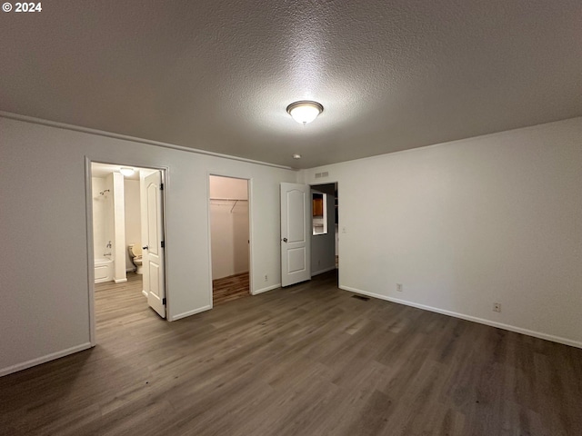 unfurnished bedroom with dark wood-type flooring, a closet, a spacious closet, and a textured ceiling