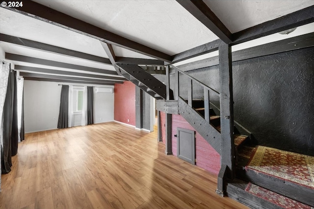 living room with an AC wall unit, beamed ceiling, and wood-type flooring