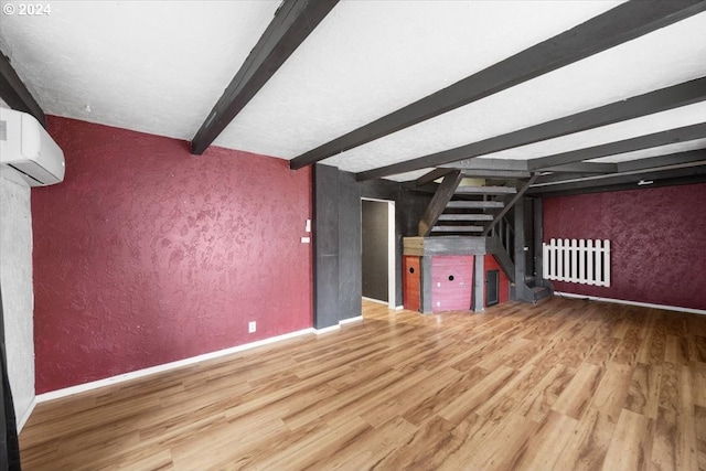 unfurnished living room featuring beamed ceiling, wood-type flooring, and a wall unit AC