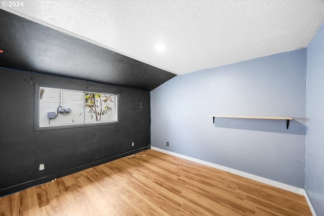 additional living space featuring hardwood / wood-style flooring, a textured ceiling, and vaulted ceiling