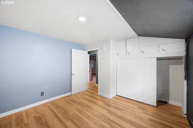 unfurnished bedroom featuring lofted ceiling, light wood-type flooring, a textured ceiling, and a closet